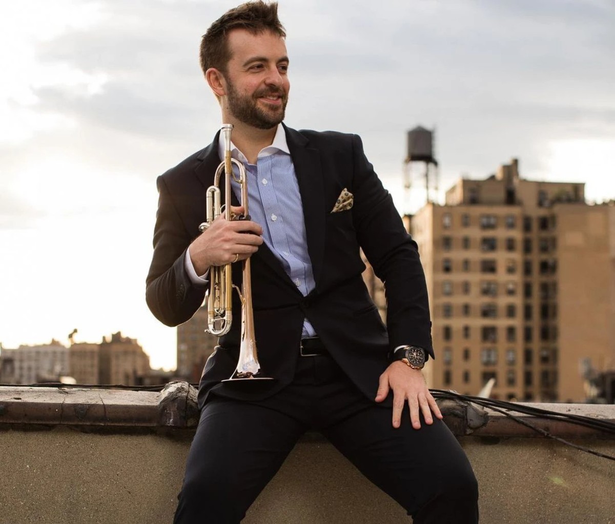 Man wearing suit sitting on rooftop with trumpet