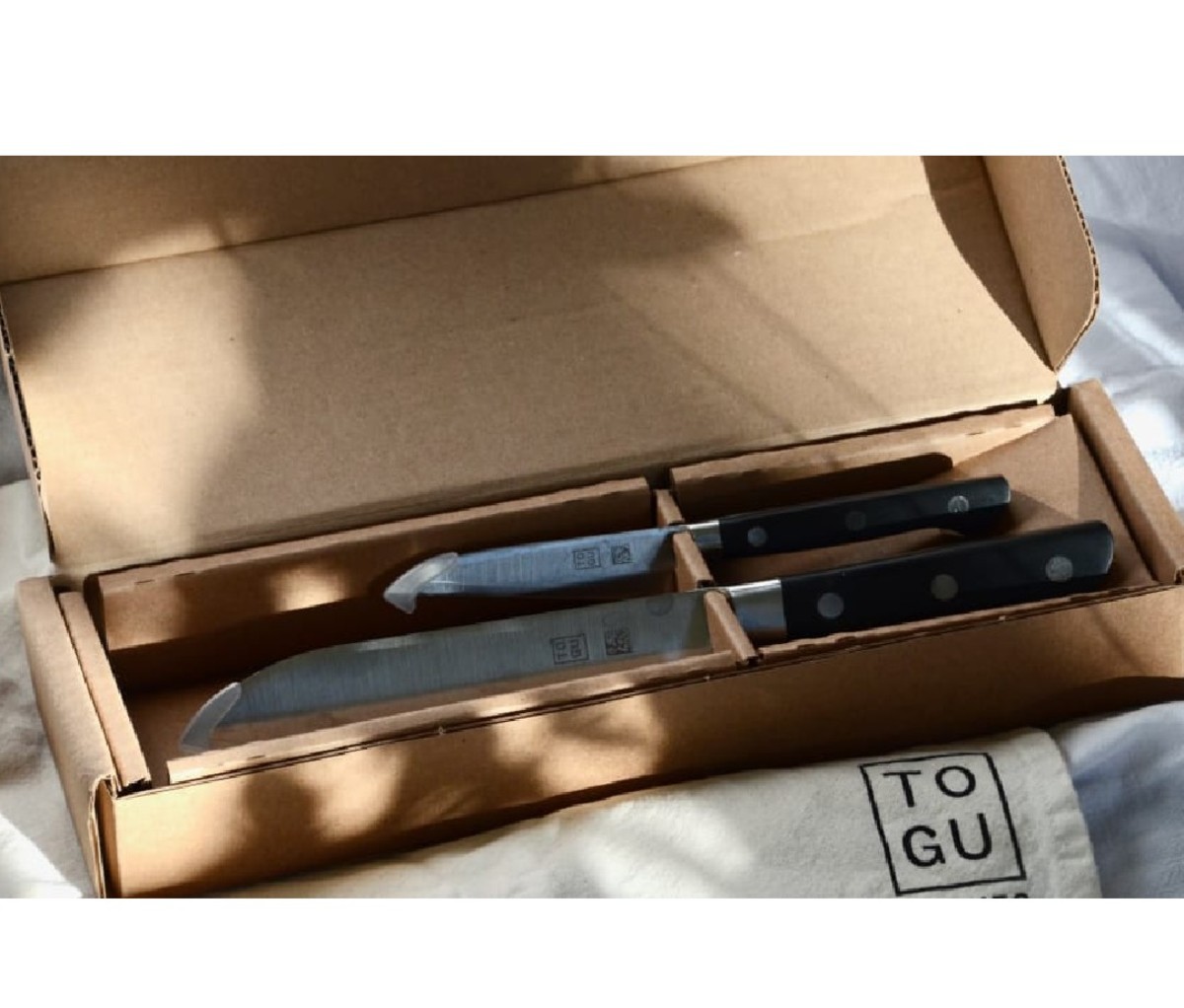 Open brown shipping box containing two Togu knives