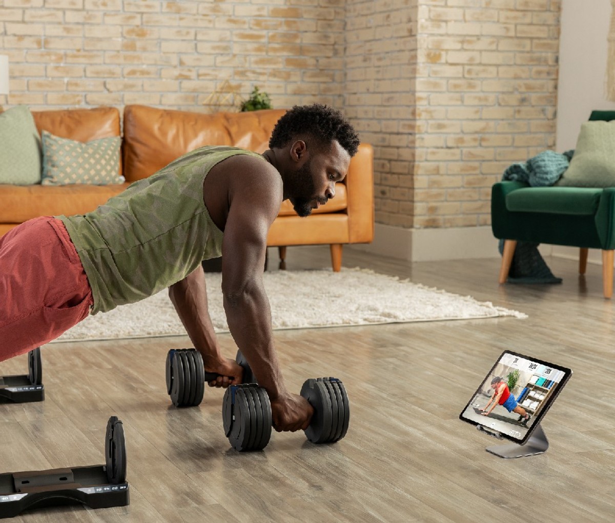 Man in pushup position with weights in front of workout class on tablet screen