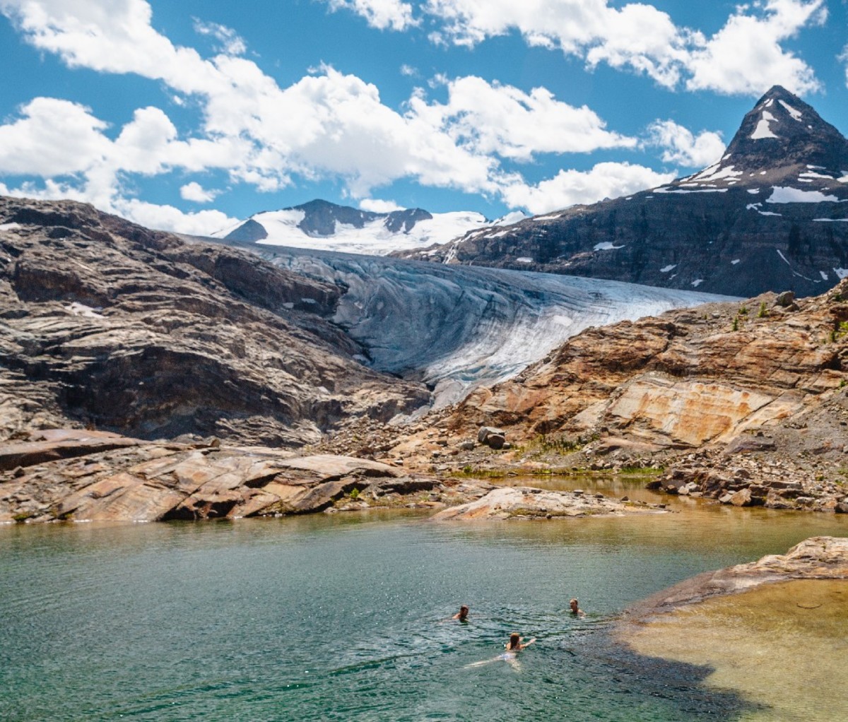 Three summer hikers swim in an alpine lake in the Canadian mountains