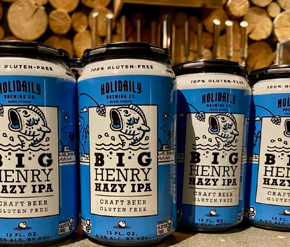 Vier blikken Holidaily Brewing Company Big Henry Hazy IPA met gesneden stammen op de achtergrond.