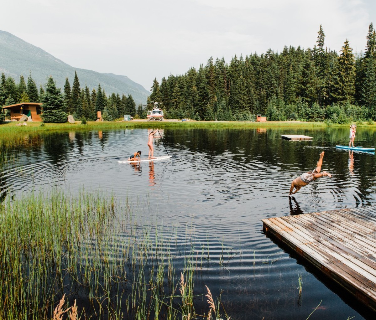 Guests recreate on a lake at one of CMH's summer lodges, paddleboarding and diving into the water.
