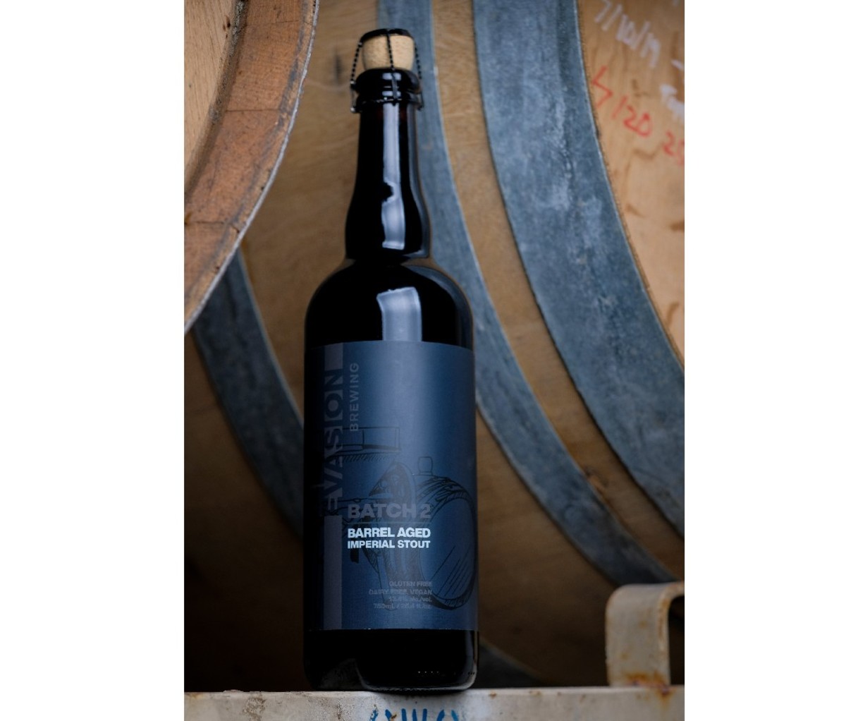 Hoge zwarte fles Evasion Brewing Batch 2 Barrel Aged Imperial Stout voor een vatwandachtergrond.