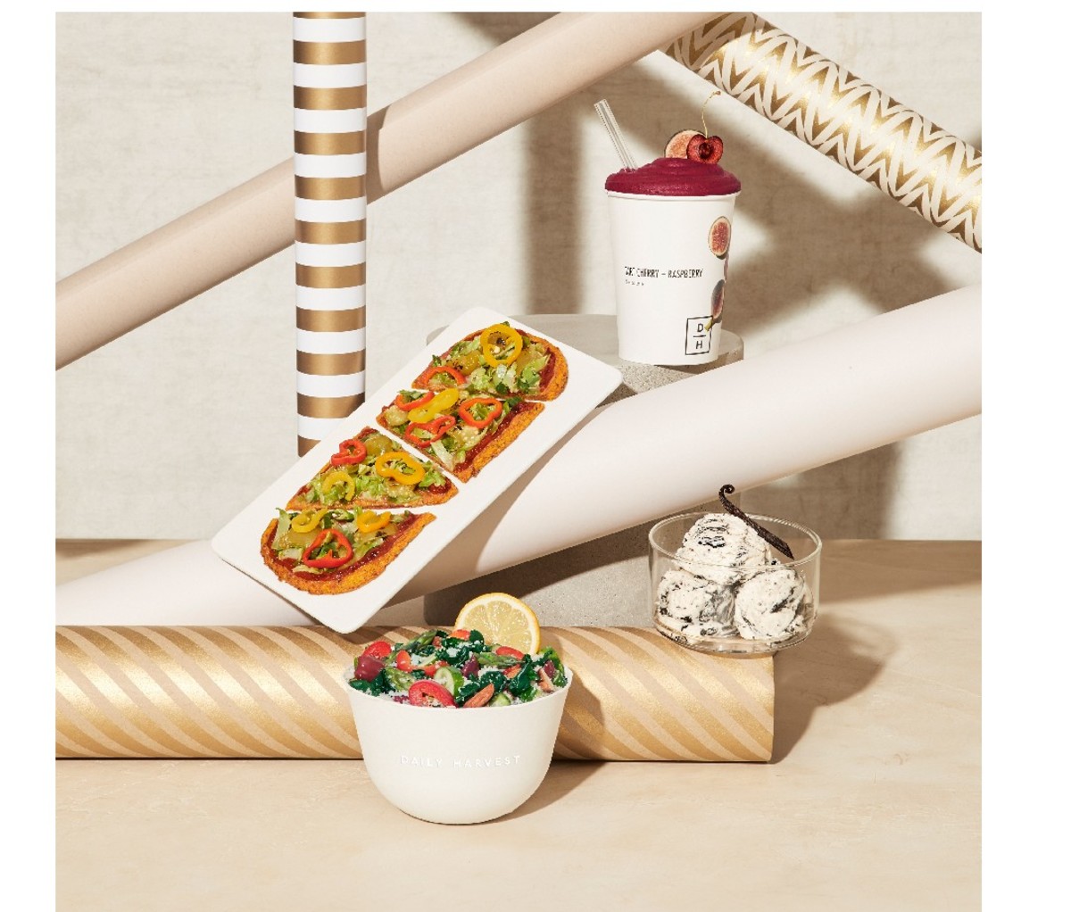 Flat bread, salad and ice cream selection for Daily Harvest Custom Gift Box displayed with rolls of wrapping paper.