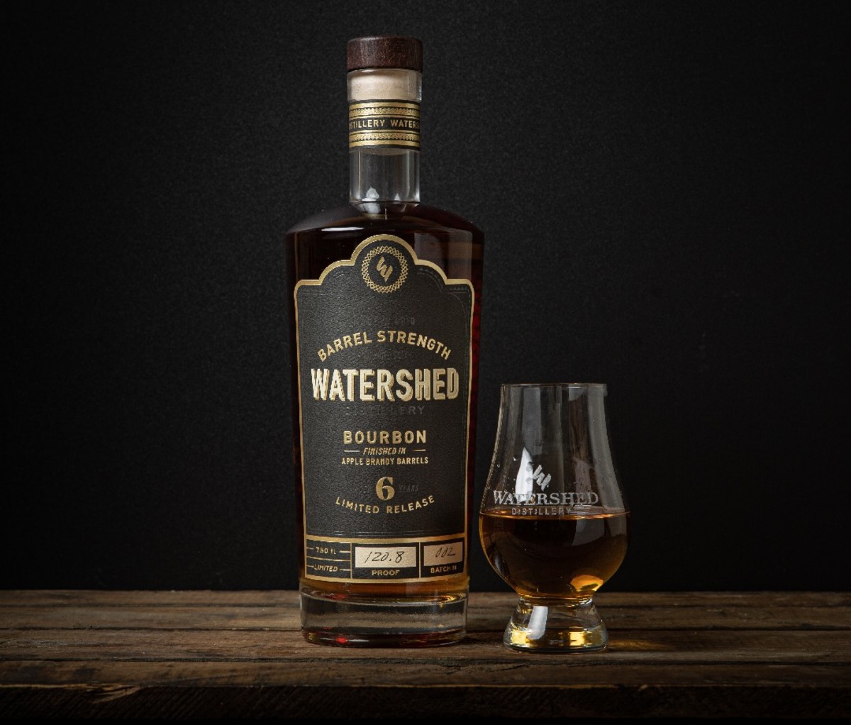 Bottle of Watershed Barrel-Strength Apple Brandy-Finished Bourbon beside a snifter of whiskey on a wooden table
