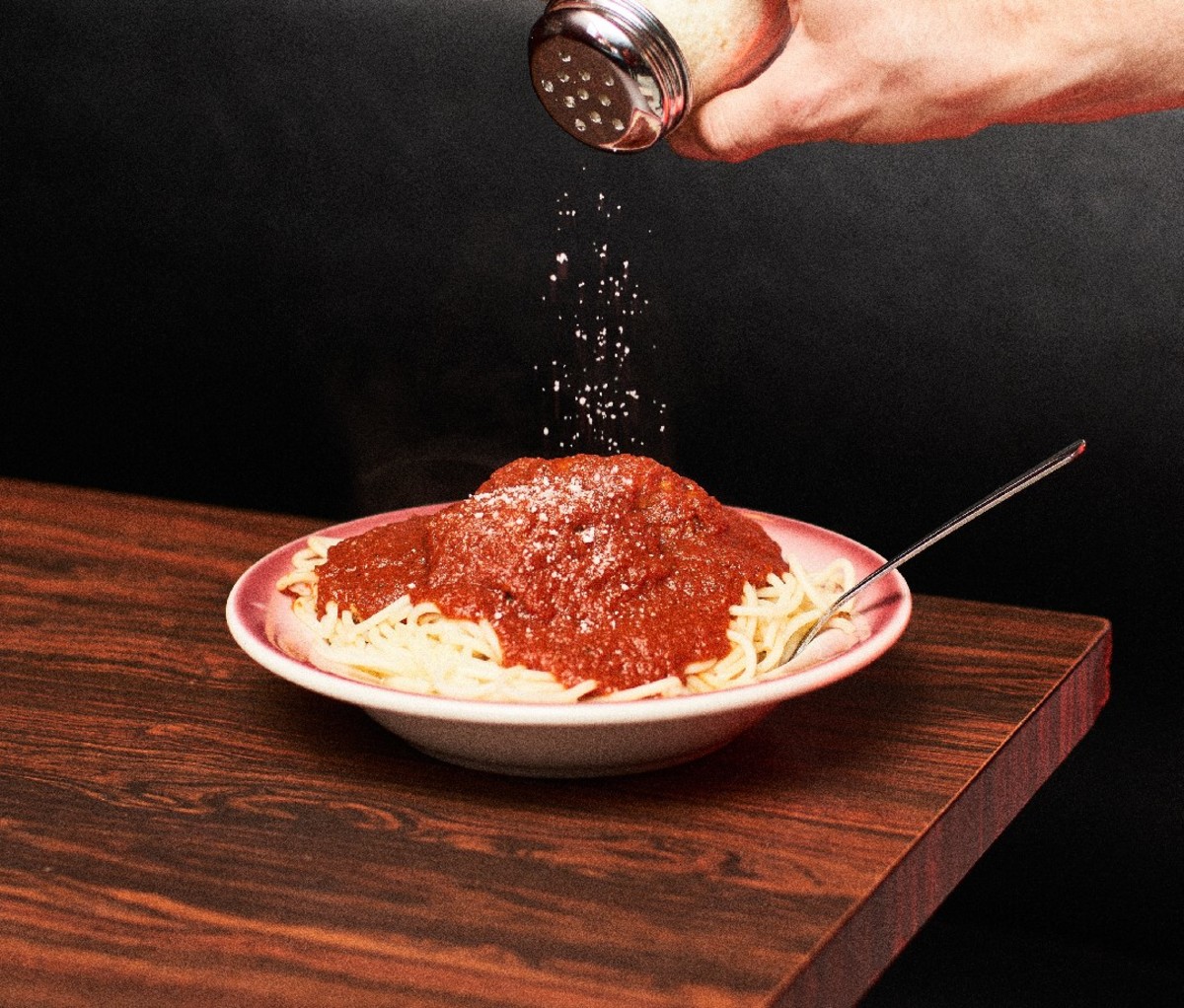 Man sprinkling cheese over spaghetti