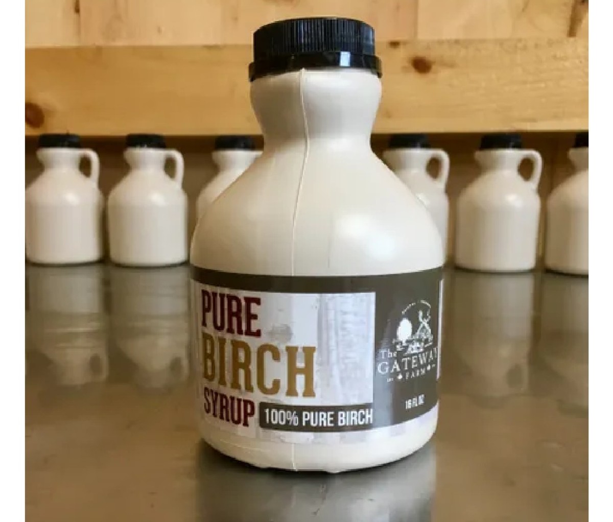 Beige bottle of Gateway Farm Birch Syrup on a table with a row of bottles in the background