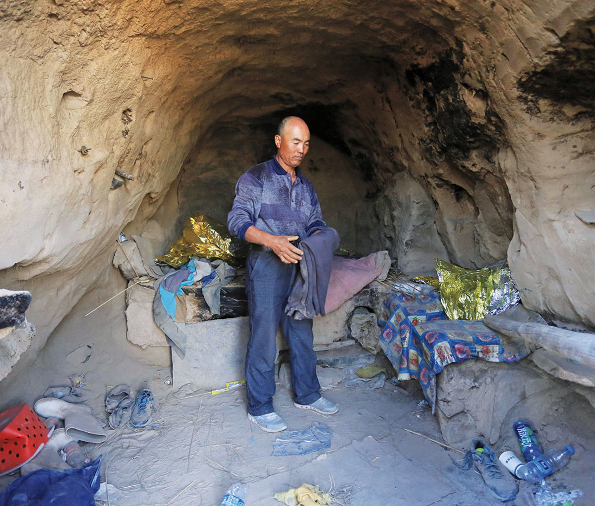 Man in cave surrounded by water bottles and debris