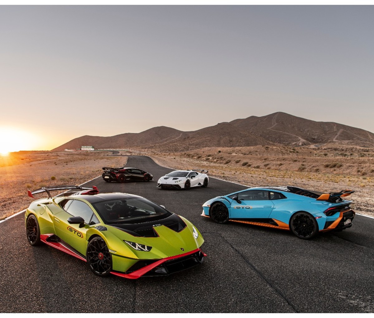 Four 2021 Lamborghini Huracán STOs parked on a race track at sunset. Colors: green, blue, white and black