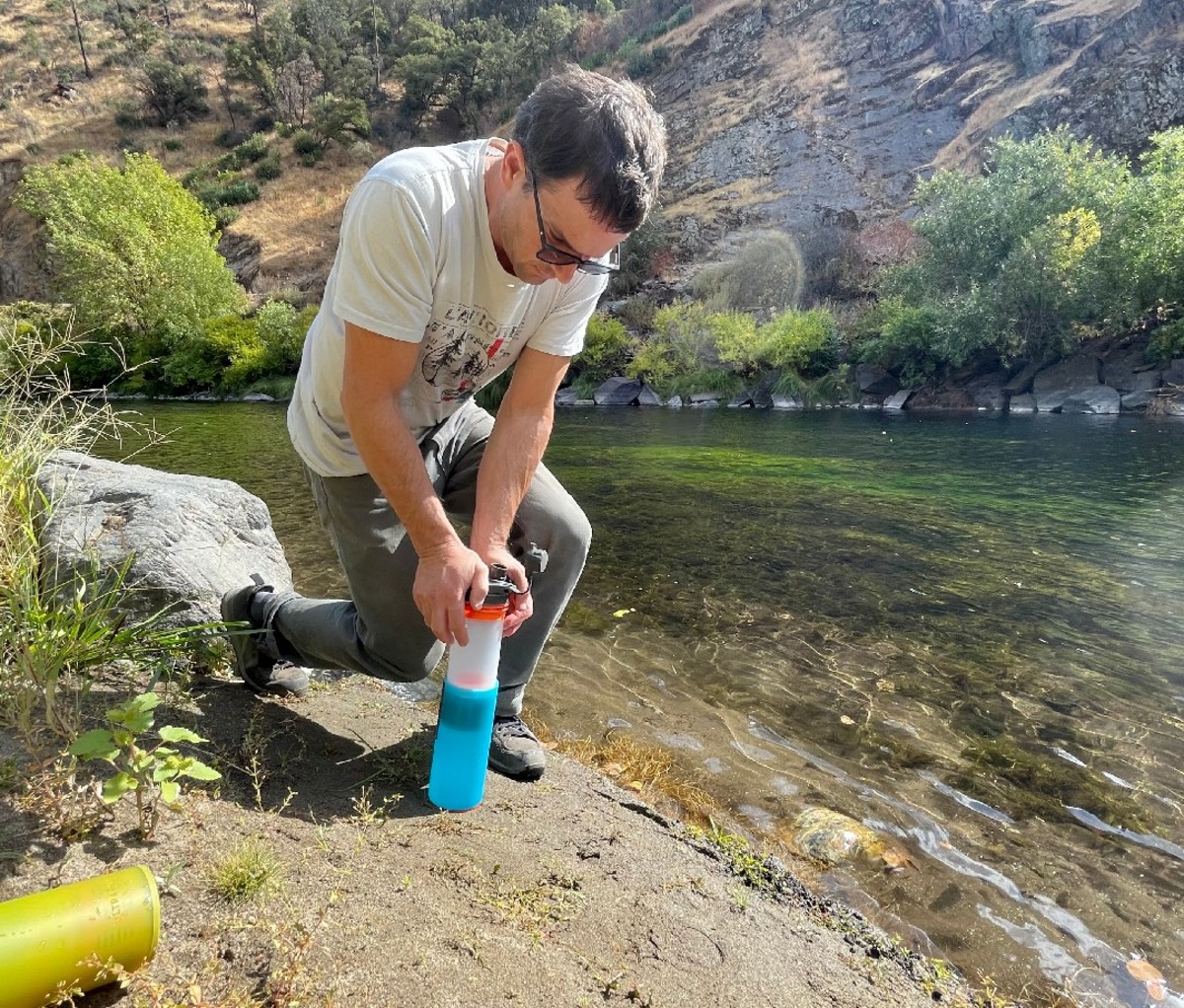 Man inserting filter into purifier bottle by streambed