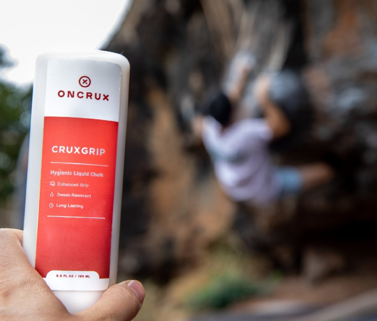 OnCrux Cruxgrip liquid chalk in hand with climber in background