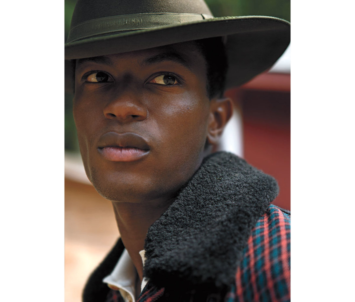 Black model wearing green hat and plaid jacket looking over shoulder