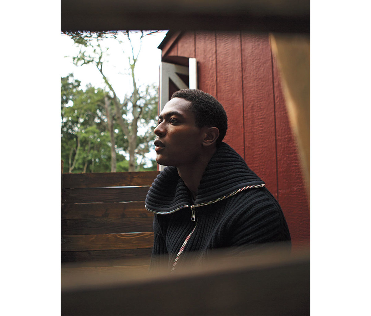 Black male model wearing funnel neck sweater outside near barn