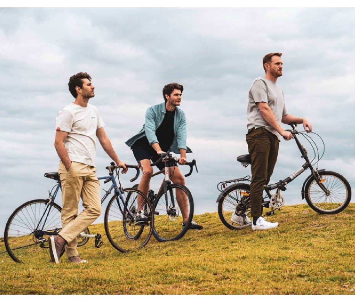 Three men on bikes on a grassy hill wearing Bottoms Lab Momentum Pants, and shorts