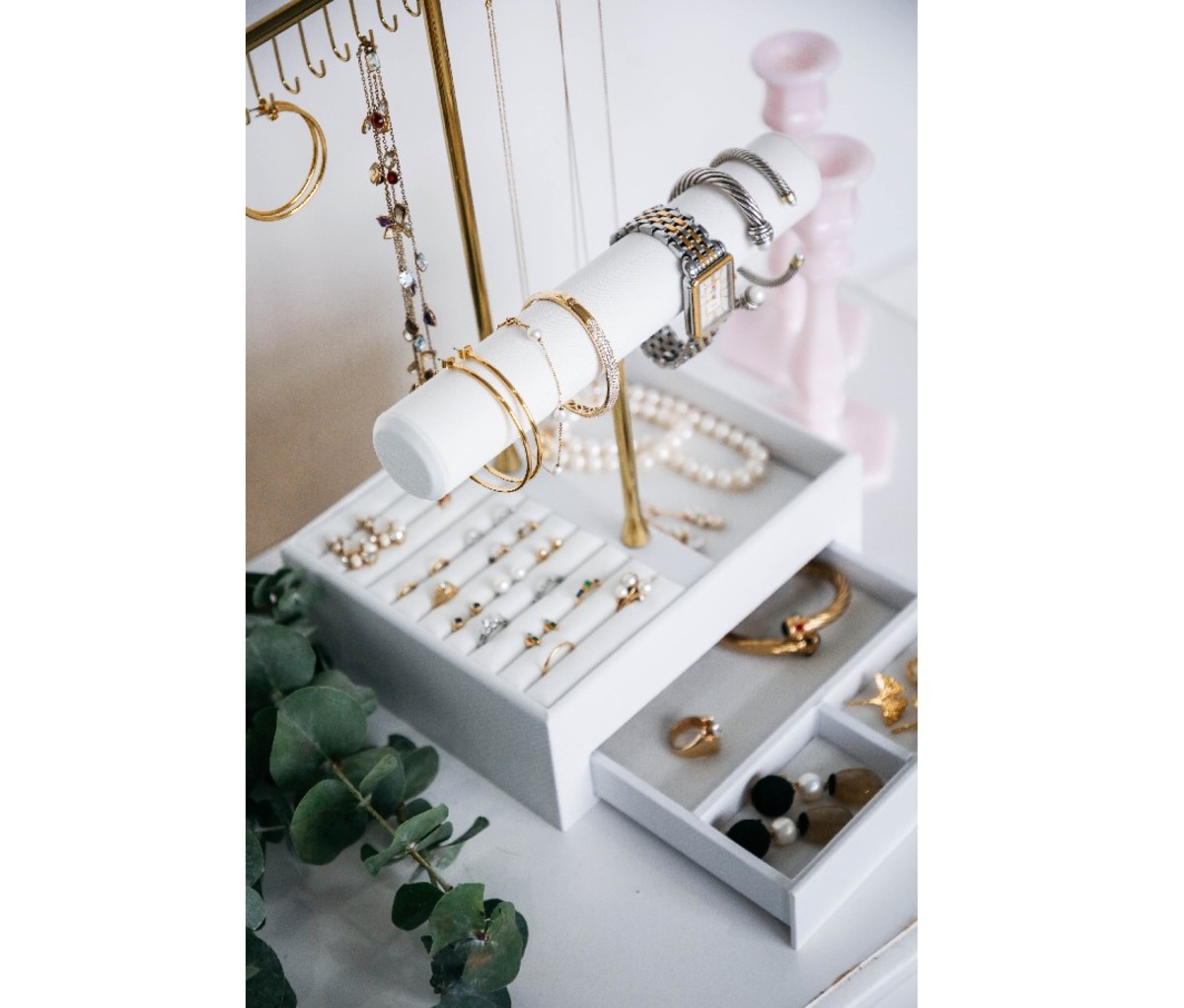 Gray Bow + Sprig Jewelry Stand adorned with hanging necklaces and other jewelry on a shelf and lower drawers