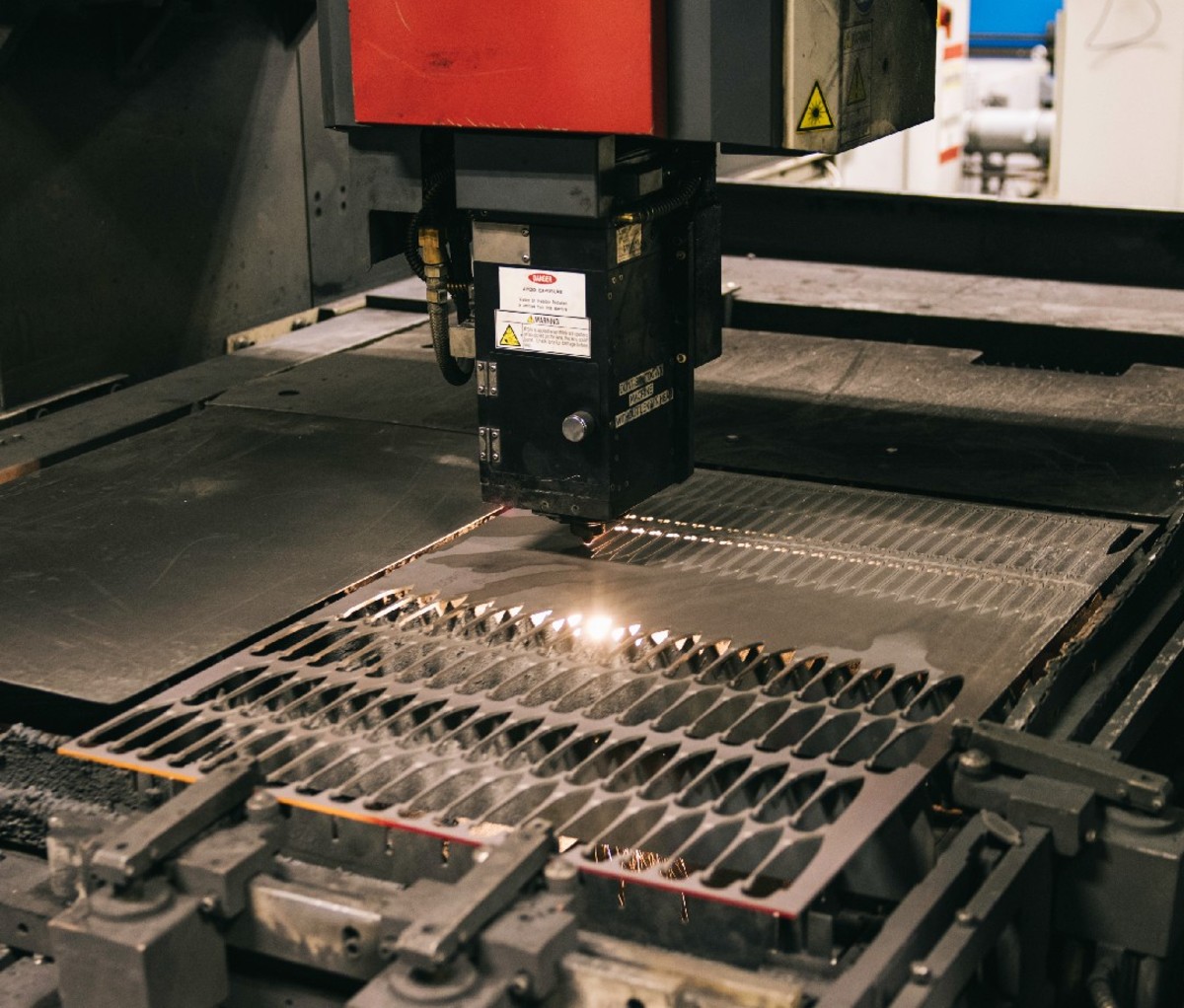 A laser machine creating blade cutouts on a horizontal steel sheet