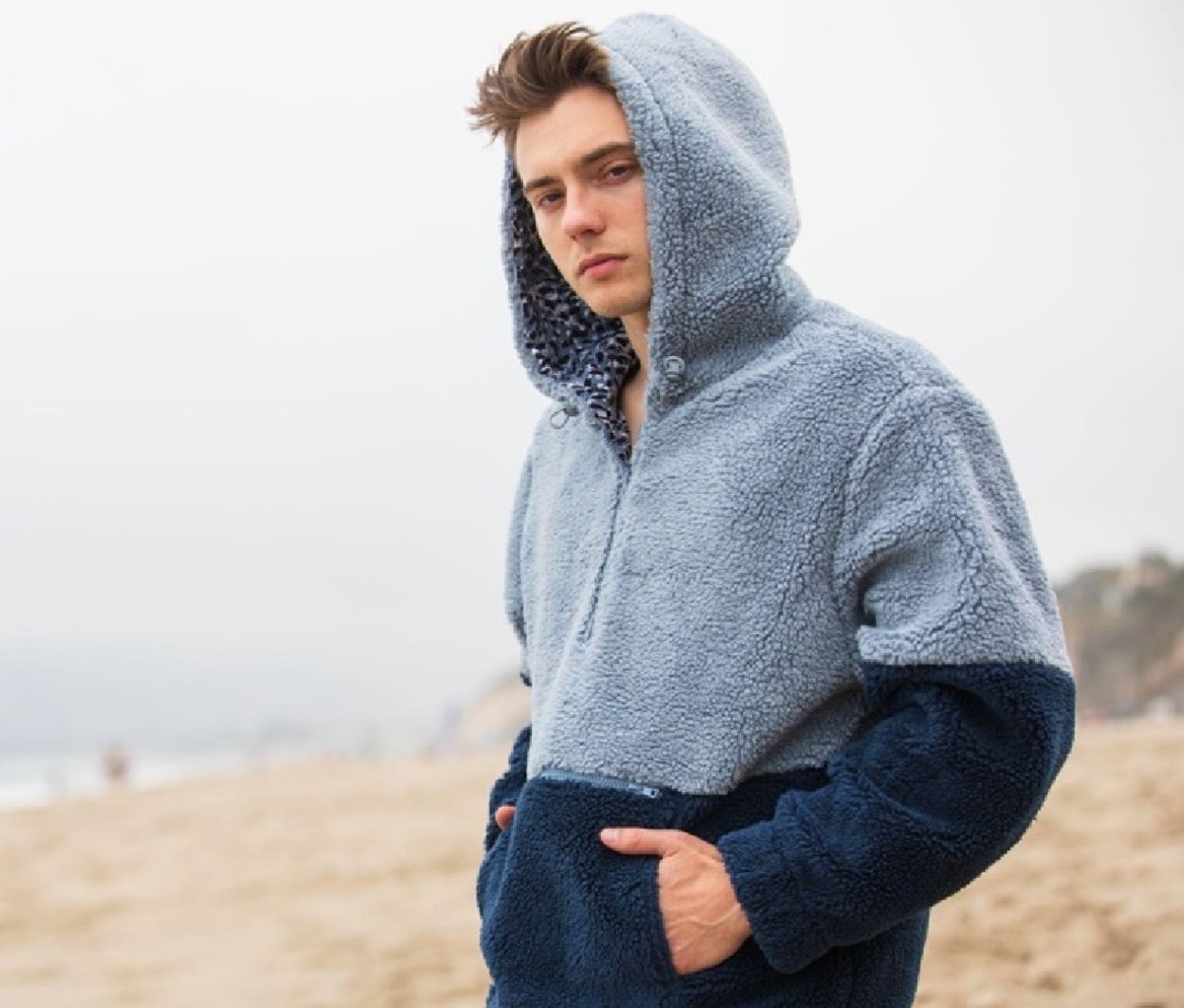 Man wearing a light-and-navy blue Eubi Reversible Teddy Borg Hoodie on the beach