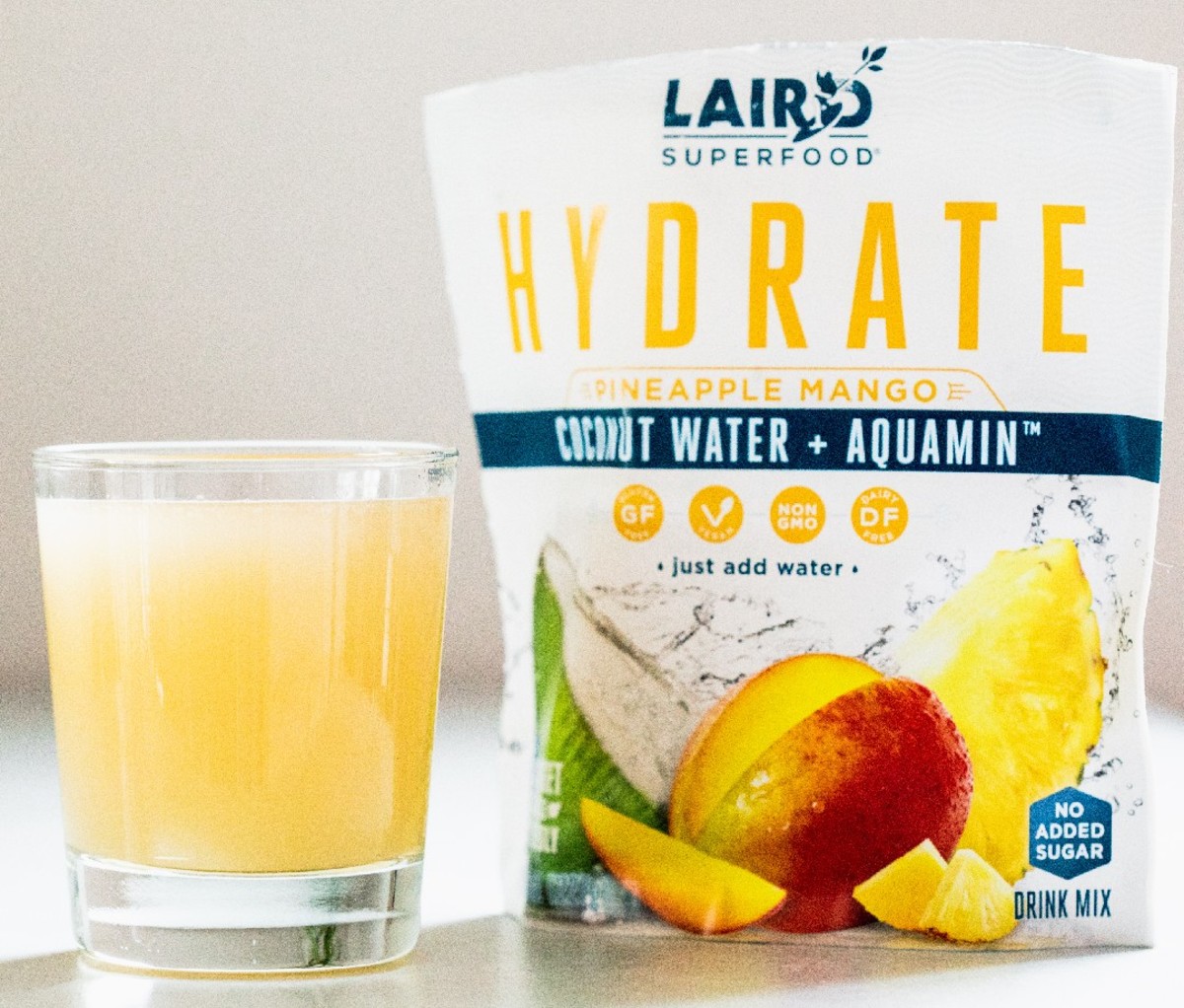 Packet of pineapple-mango flavored Laird HYDRATE powder next to a full glass of it