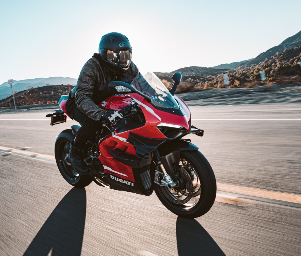 Side view of a rider on a red 2021 Ducati Superleggera V4 motorcycle on a flat two lane highway