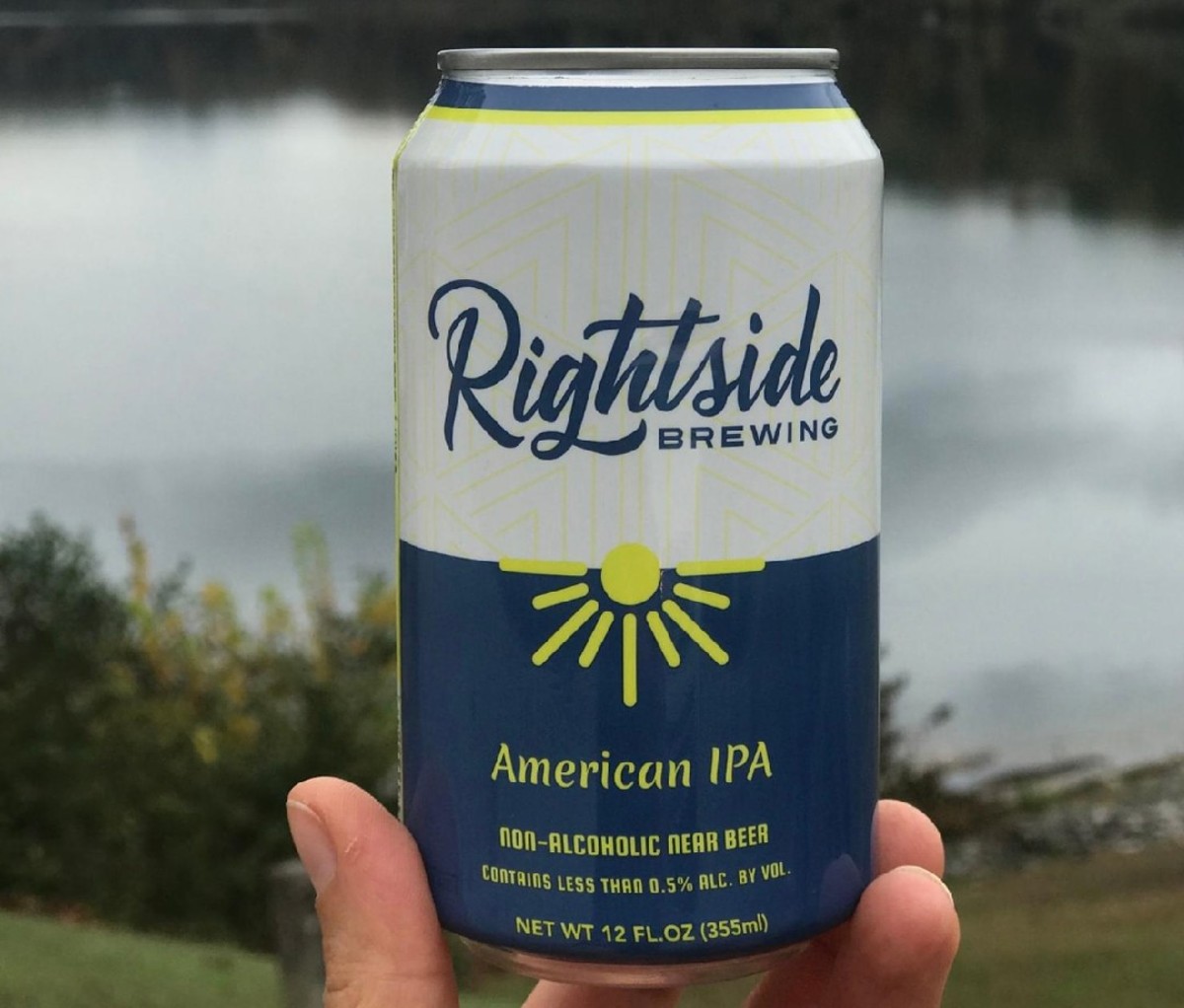 Closeup of hand holding a 12 oz can of Rightside Brewing IPA with a scenic lake background