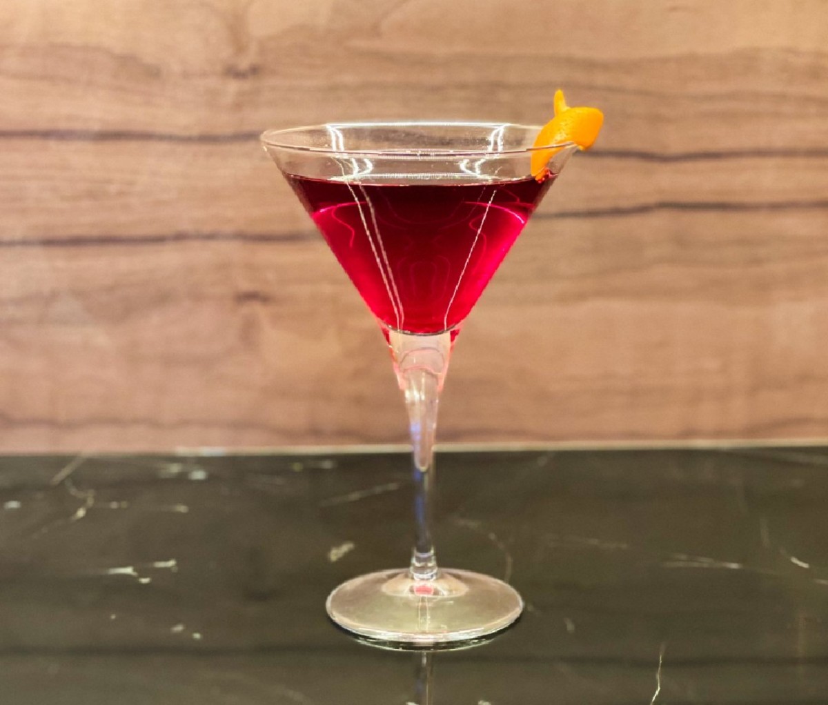 Reddish-colored yuzu martini with an orange twist garnish