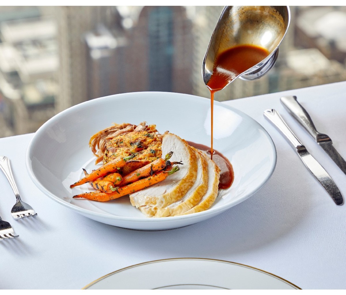 Sliced turkey dinner on a plate with gravy being poured from above with Signature Room window view in the background