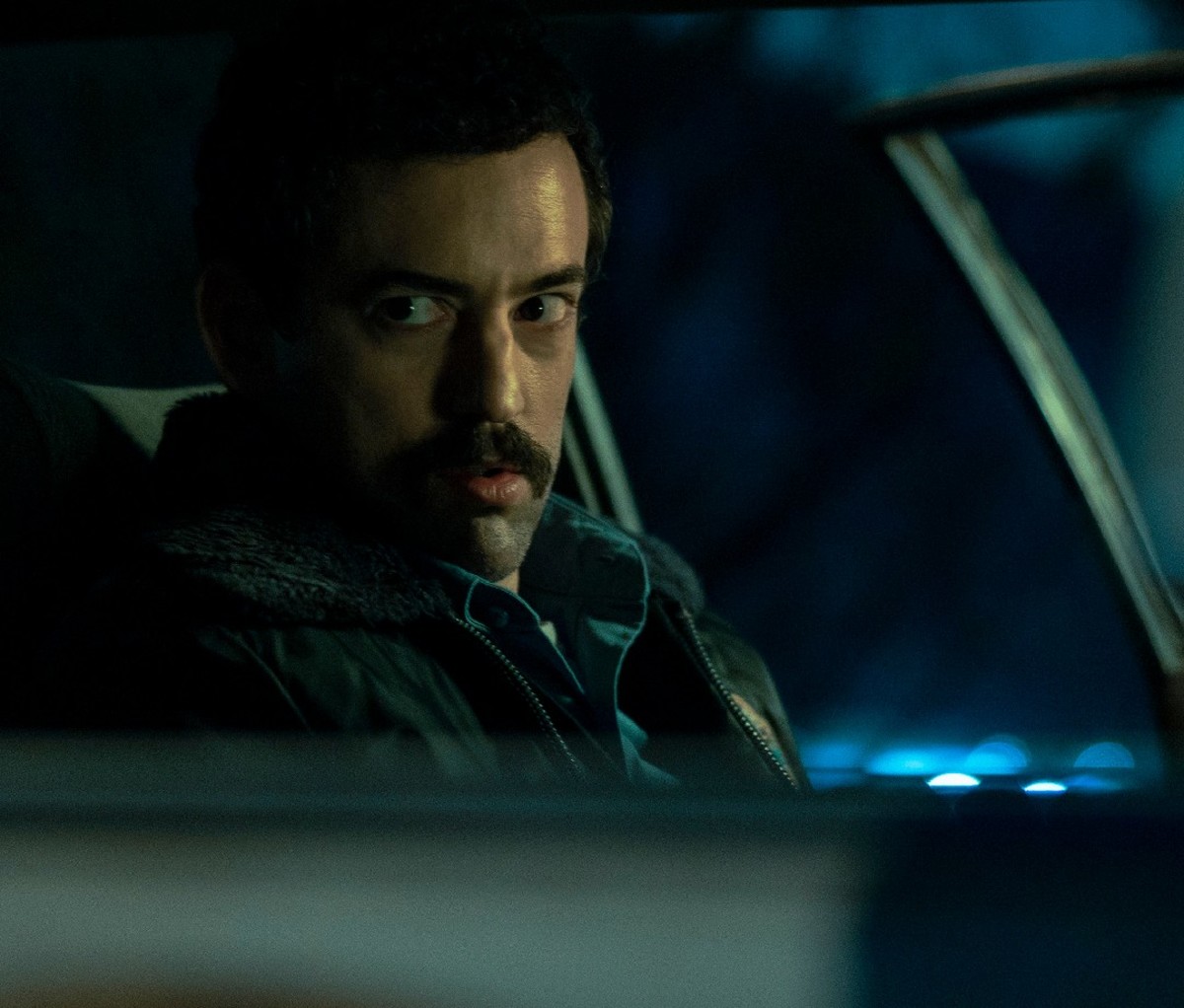 Dunkle Nahaufnahme von Narcos: Der mexikanische Schauspieler Luis Gerardo Méndez sitzt nachts in seinem Polizeiauto