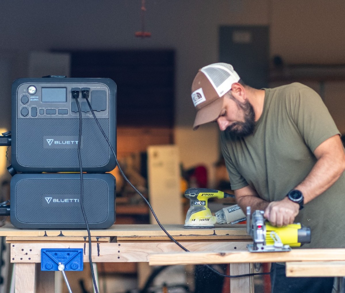 Man using a power tool in a wood workshop with Bluetti portable power station beside him
