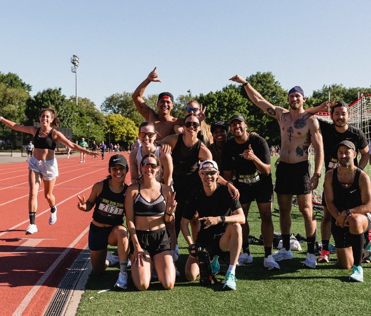 Group of men and women posing for photo next to female running on track