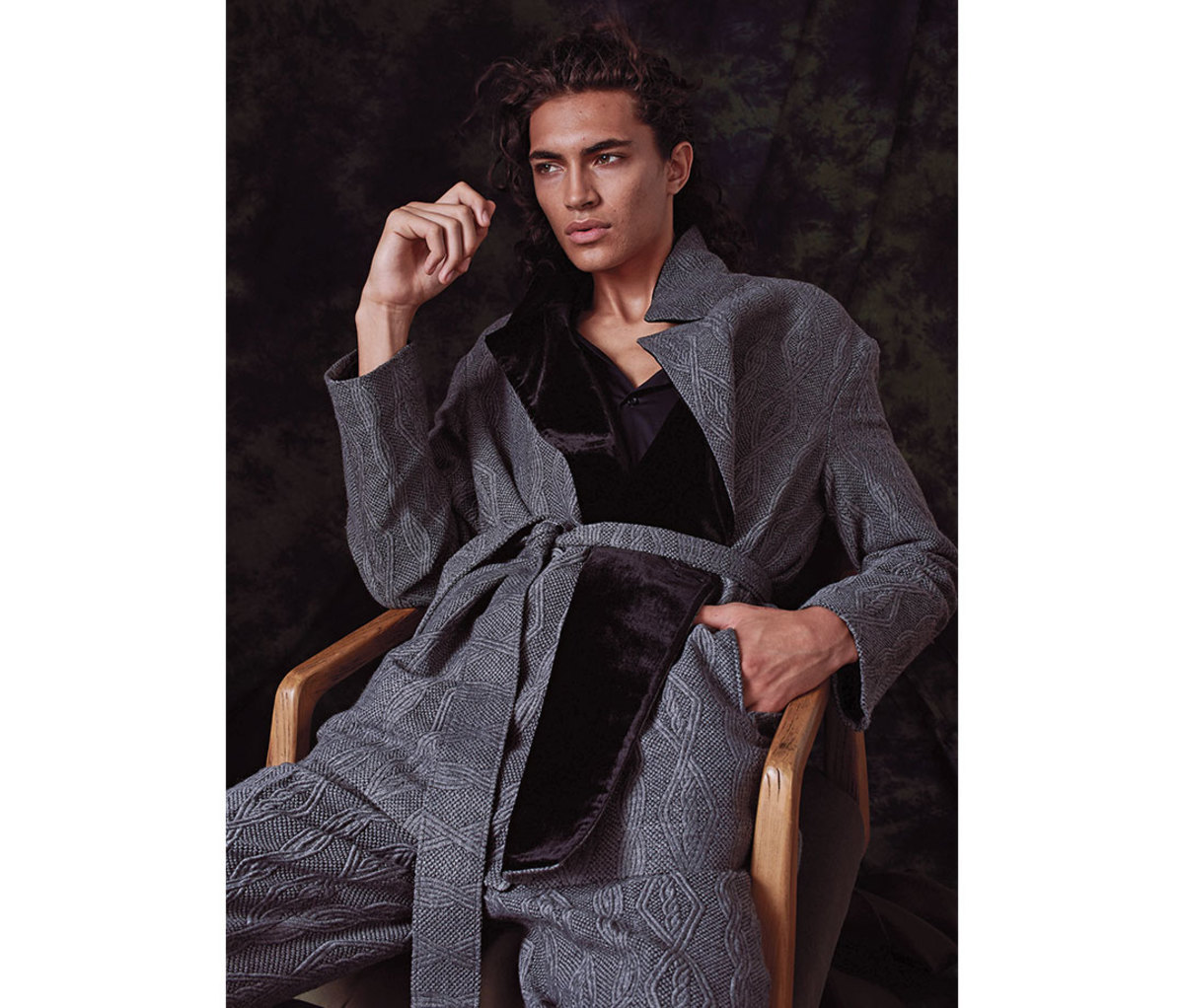 Man with shoulder-length hair sitting in chair wearing belted jacket