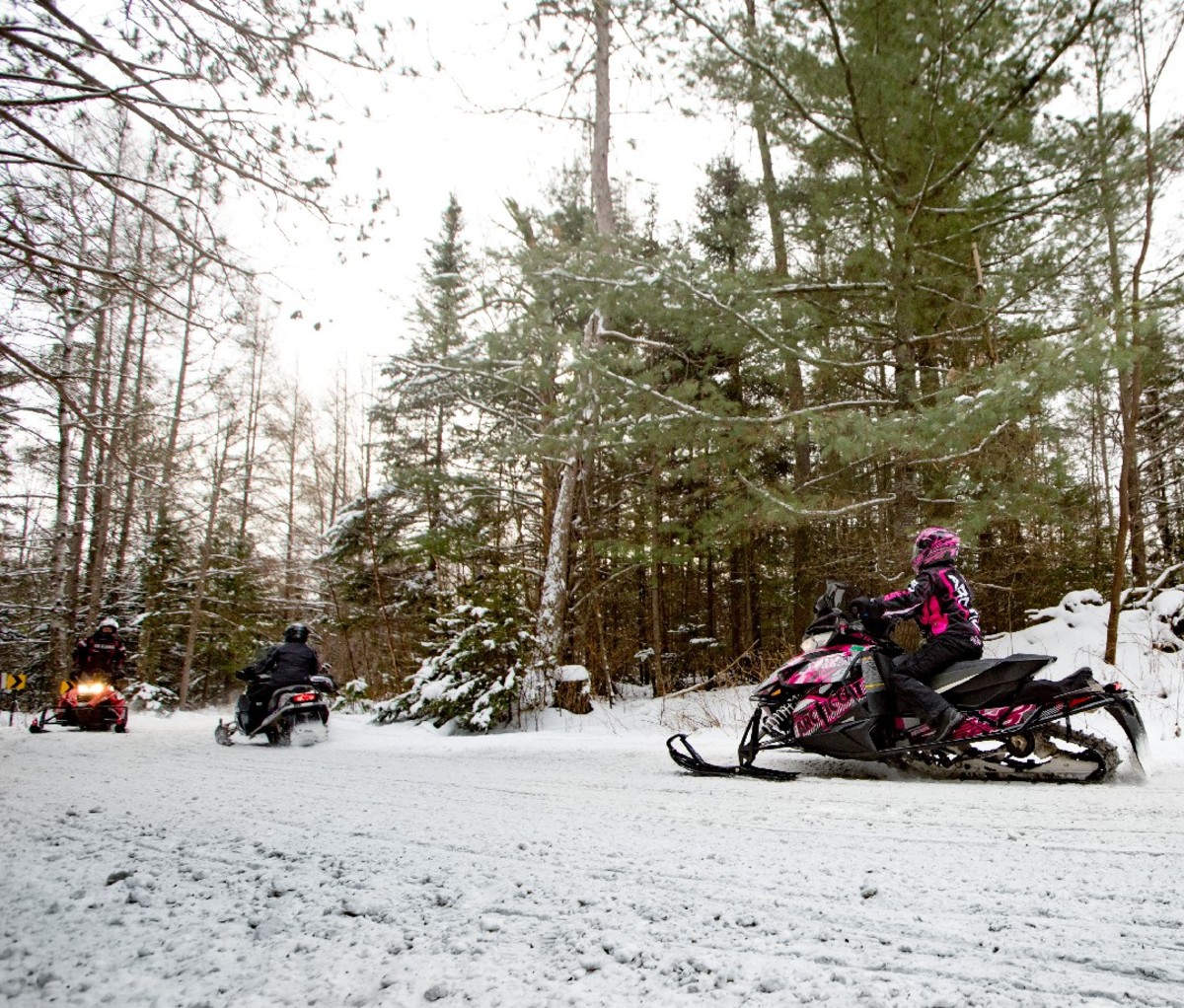 Snowmobile riders on a snowmobile trail through the trees in Eagle River, Wisconsin