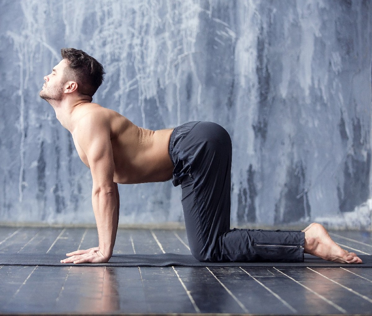 Man doing yoga cat pose in front of a gray wall