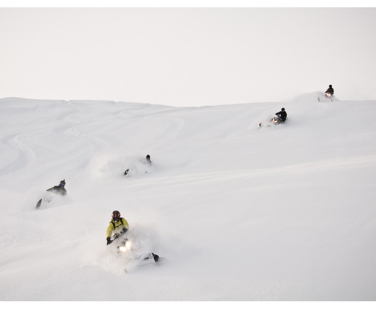 Group of snowmobilers winding down a powdery hill in Revelstoke, British Columbia.