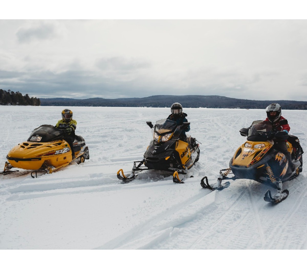 Three snowmobilers riding along a flat, open trail in the Maine Highlands