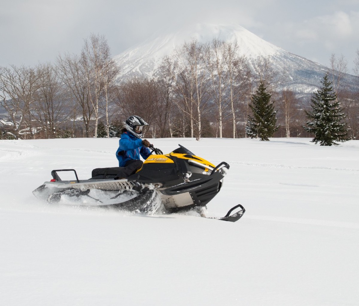 Snowmobiler riding on a snowy flat in Hokkaido, Japan with conical volcanic peak Mount Yotei in the background
