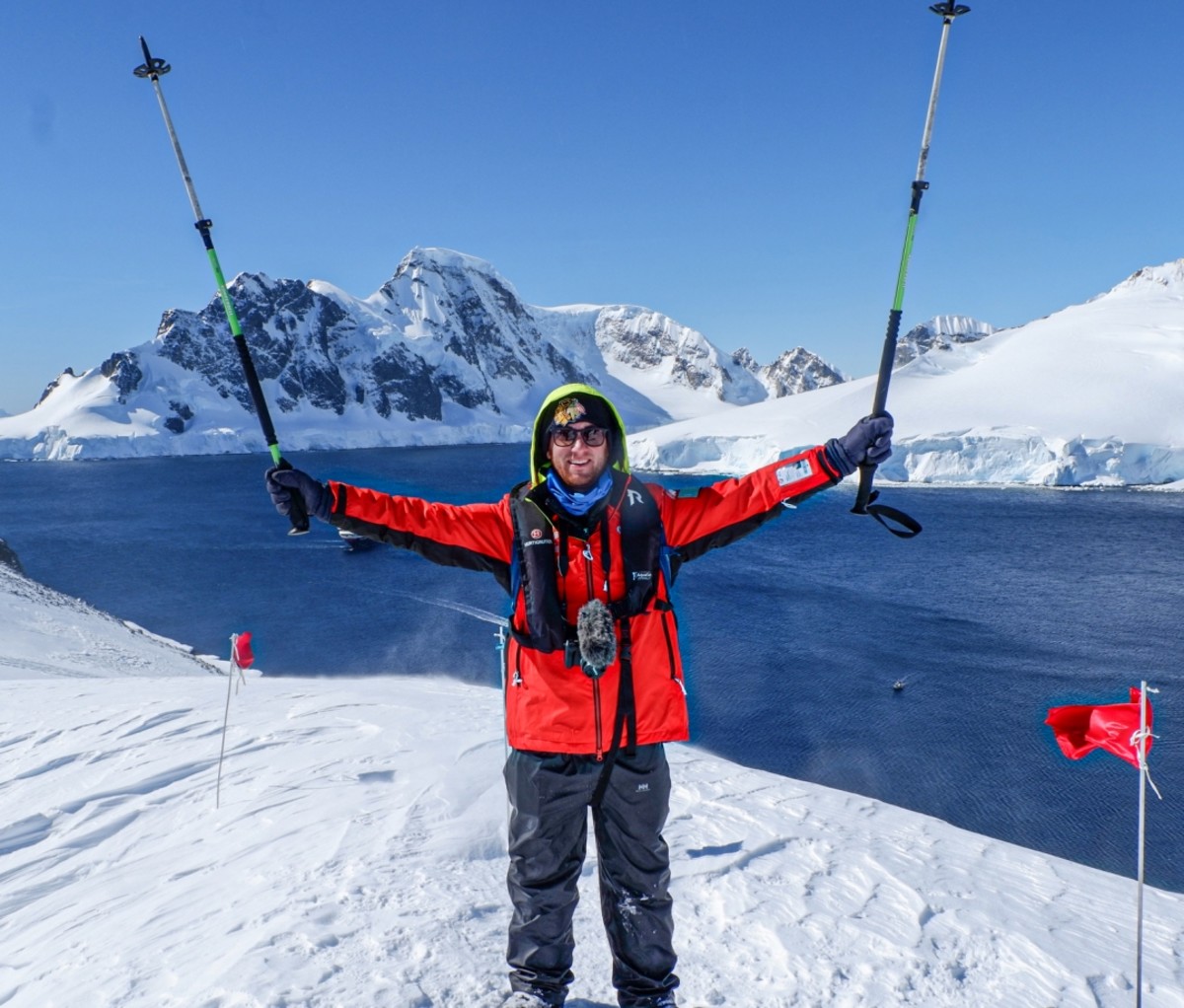 Drew Binsky in a red winter jacket standing on top of a snowy mountain