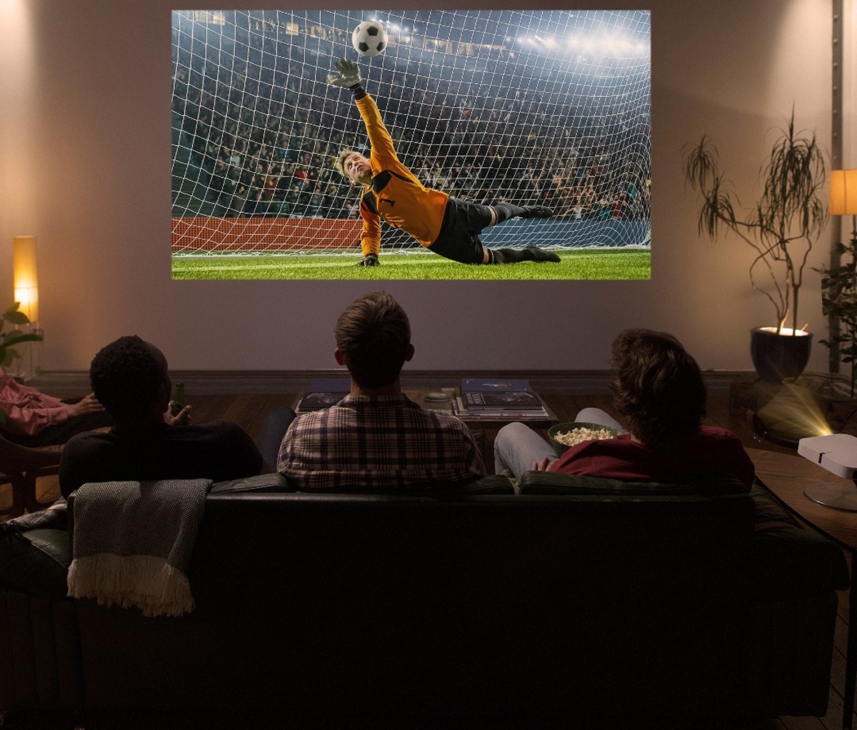 Three men sitting on couch watching soccer game off projector