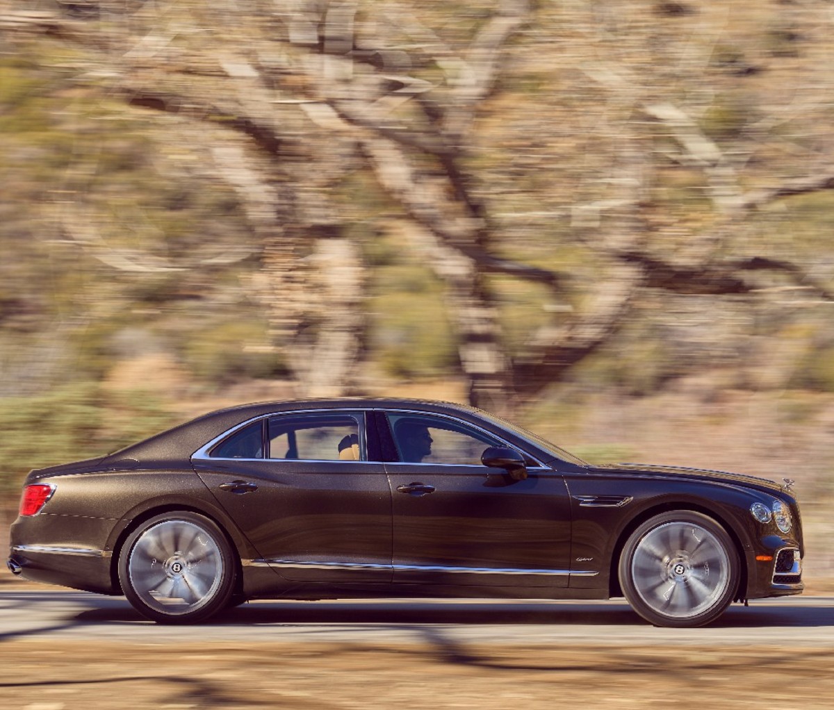 Black 2022 Bentley Flying Spur Hybrid on a treelined road, side profile