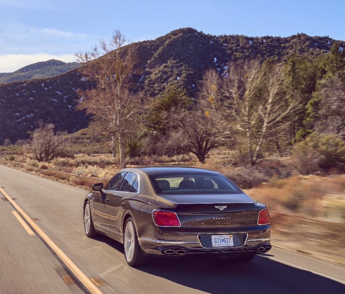 Black 2022 Bentley Flying Spur Hybrid driving on desert road, rear view