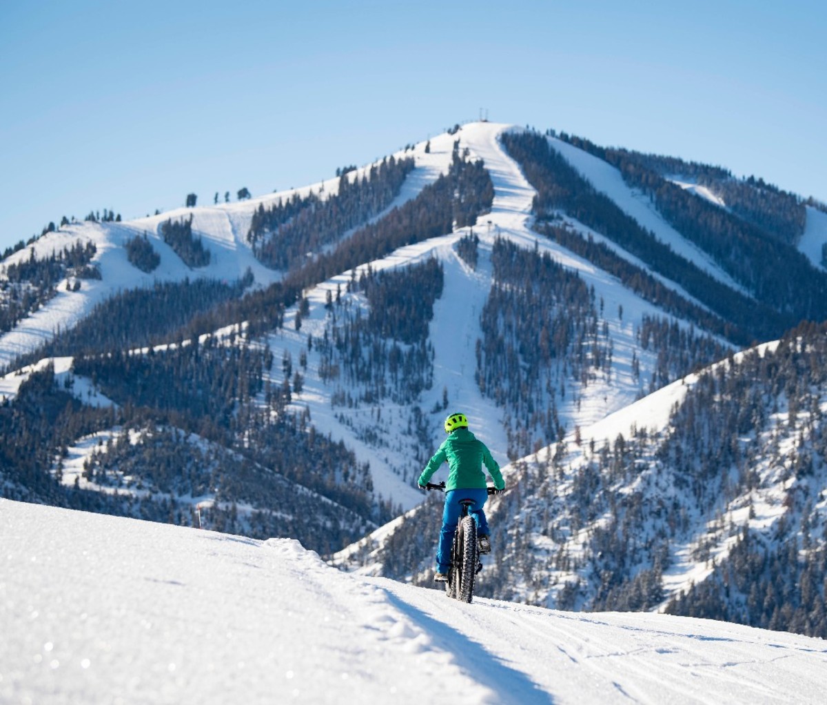 Fat biker pedalling on a snowy trail with Idaho's Sun Valley Ski Resort in the background