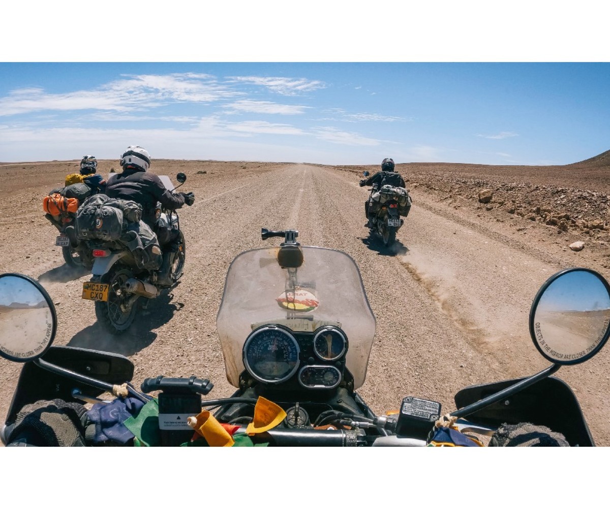 Motorcyclists riding through the desert on a long straight dirt road