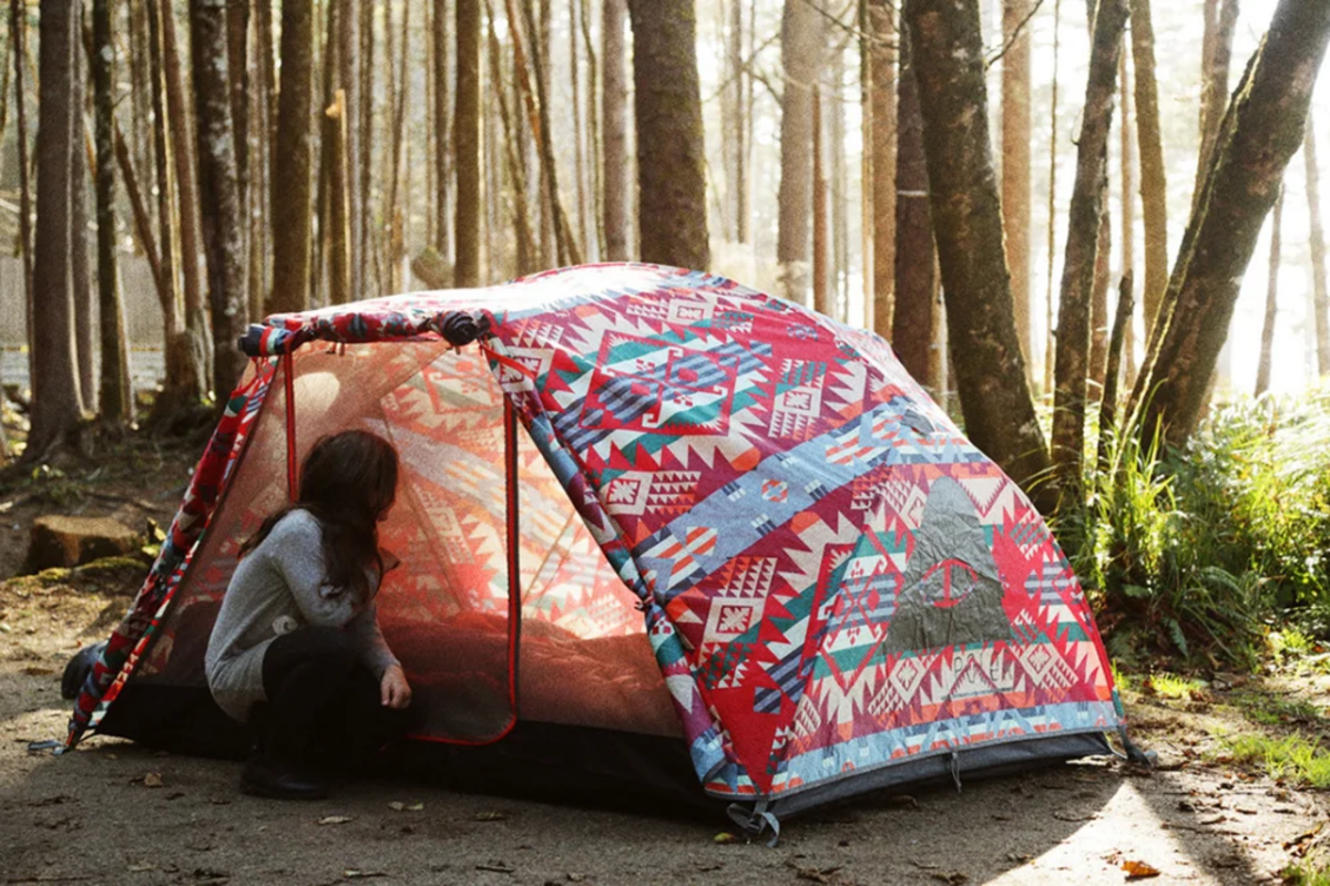 Woman kneeling inside a colorful Poler tent set up in the trees