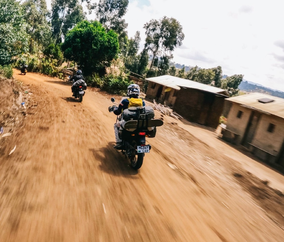 Motorcyclists ride along a dirt road through a village along their Kili-to-Cape Town route