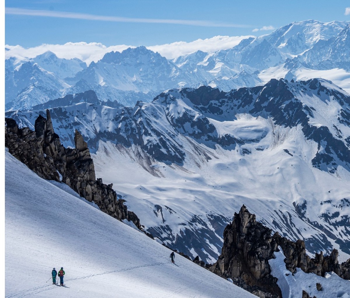 Heli-skiers stand on an upper slope overlooking a giant Alaskan mountain panorama
