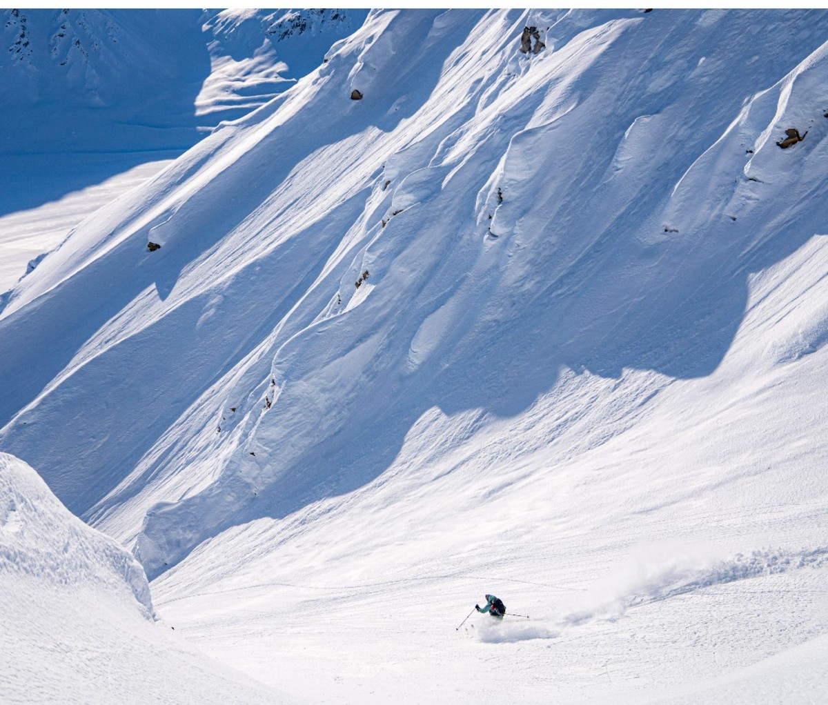 Heli-skier skiing through a powdery gully