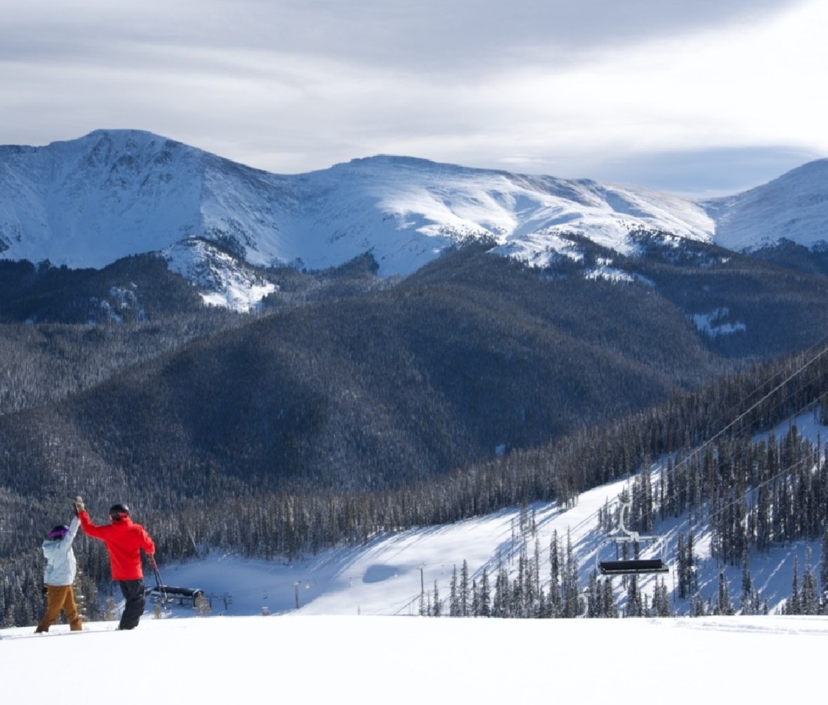 Two skiers high-five at the top of a Winter Park ski run.