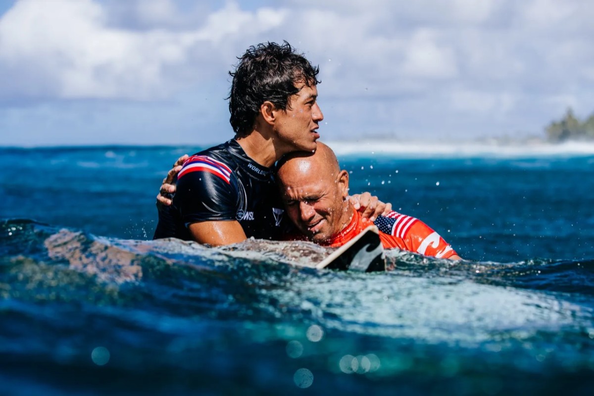 An emotional Kelly Slater embraces a surf competitor in the ocean.