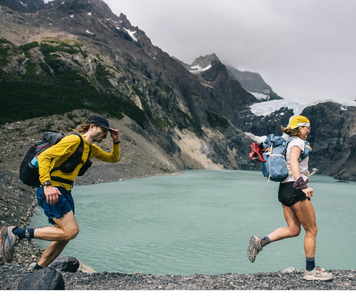 Two fastpackers jog beside a mountain-lined lake in Torres del Paine National Park