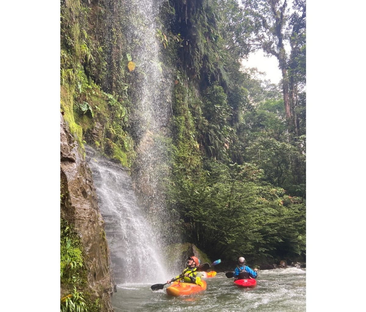 Two kayakers float on the river at the foot of a cliffside waterfall in Ecuador