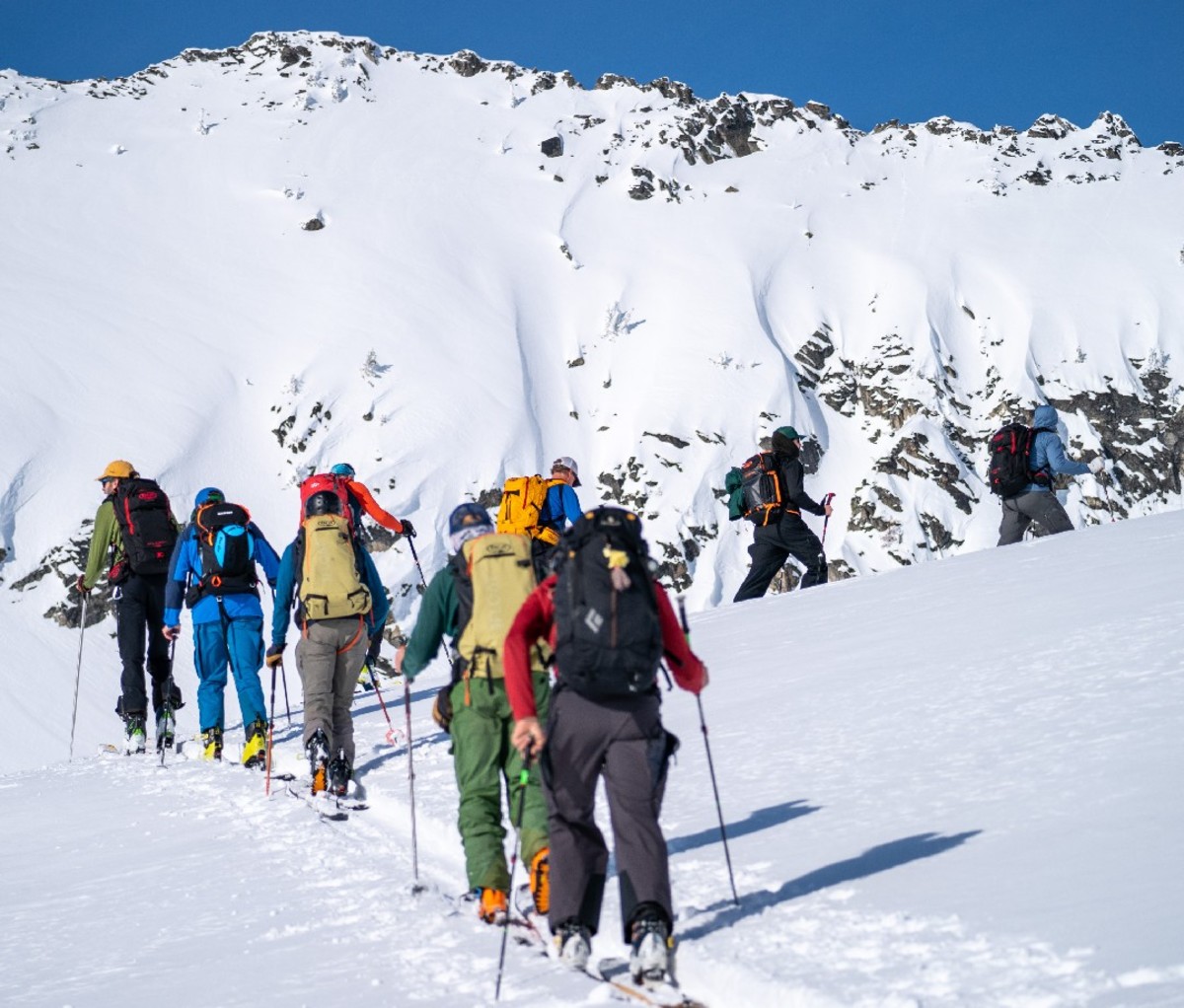 Single file row of backcountry skiiers skinning up a slope